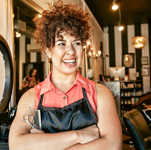 Female beauty salon owner standing with arms crossed and holding a comb and hair cutting scissors.