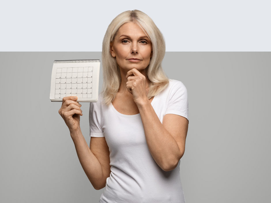 A pondering woman holds a small calendar.
