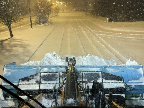 View from inside snow removal equipment of plow clearing snow-covered road during snow storm