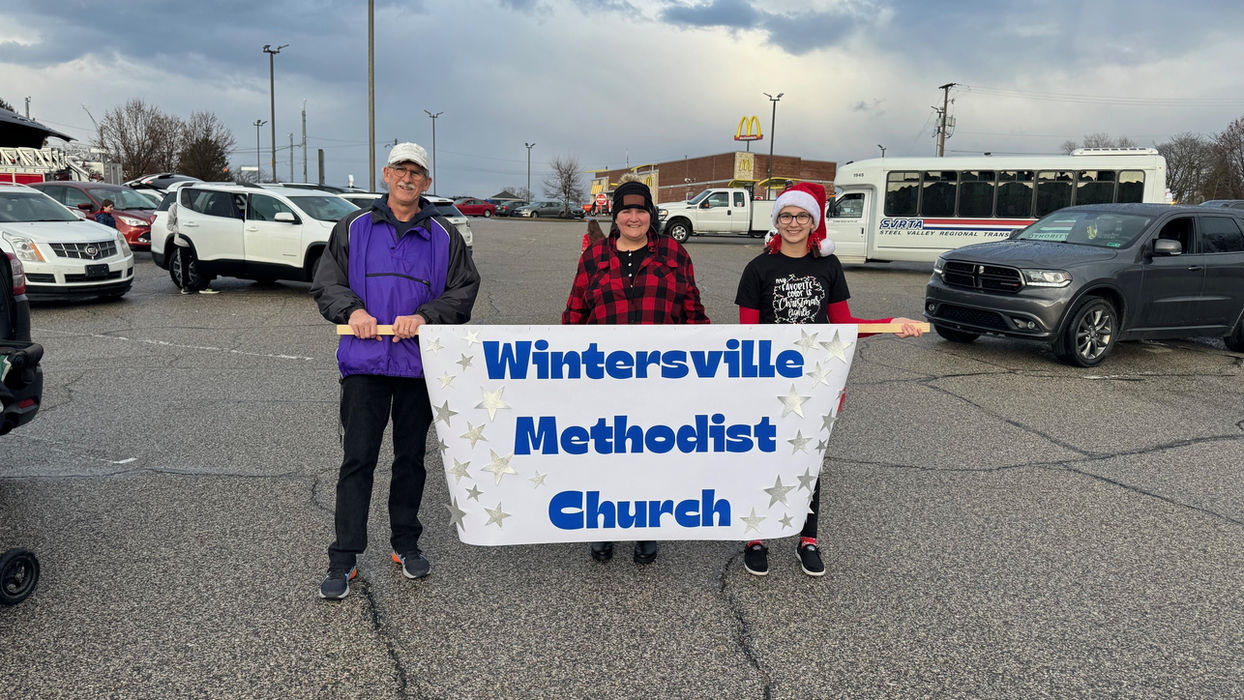 Pastor, youth coordinator, and youth ministry member standing in parking lot holding church parade banner awaiting start of event