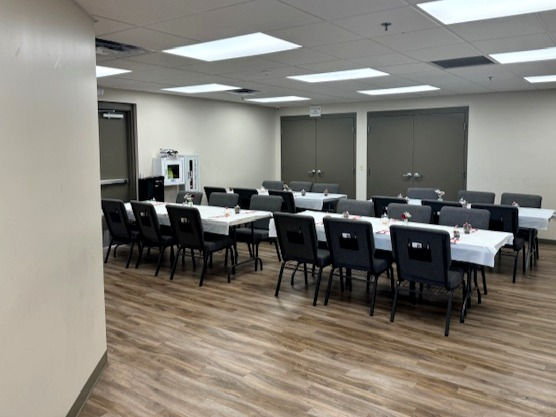 Four rectangular tables with white table covering and cushioned chairs et-up in meeting room with modern wooden flooring