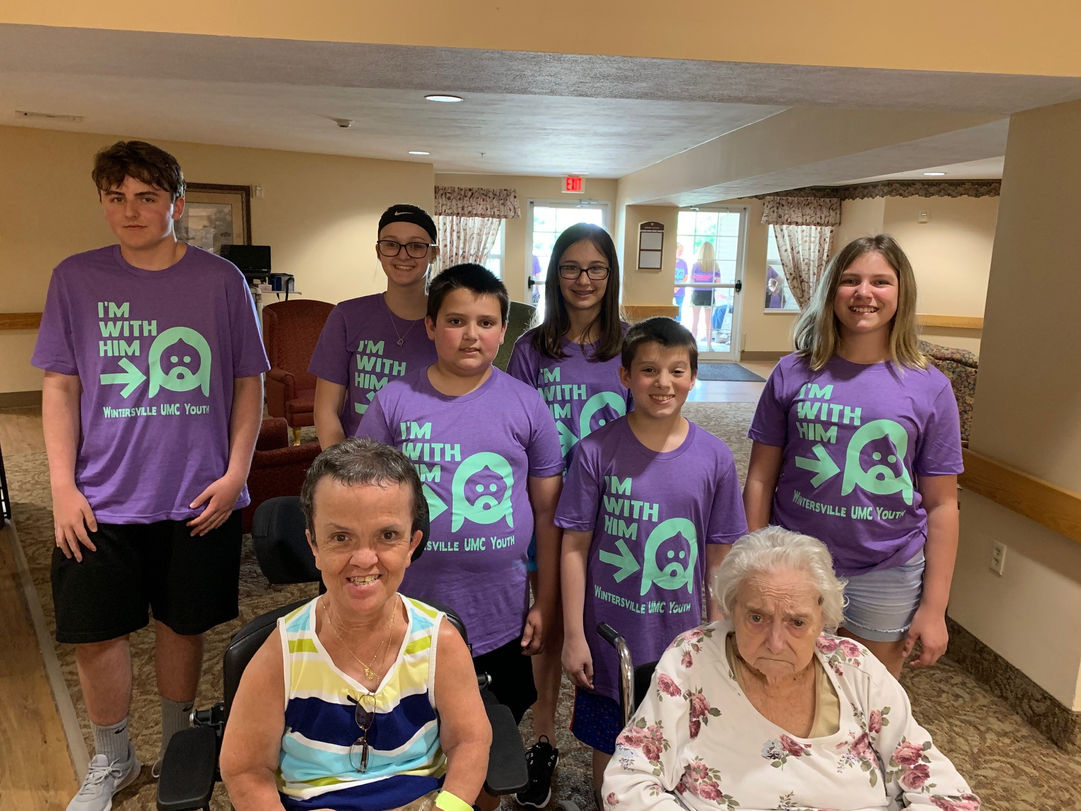 Several members of the church youth standing with two elderly individuals during home visits