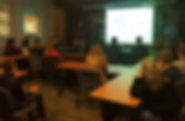 High school students watching an on screen presentation while sitting in a classroom listening intently to a professional engineer give a presentation