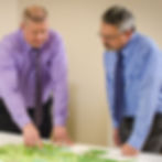 Two professionals leaning over a table while reviewing engineering plans