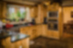 Modern and clean kitchen with lightly-colored wooden cabinetry, black marble countertops, and stainless steel appliances