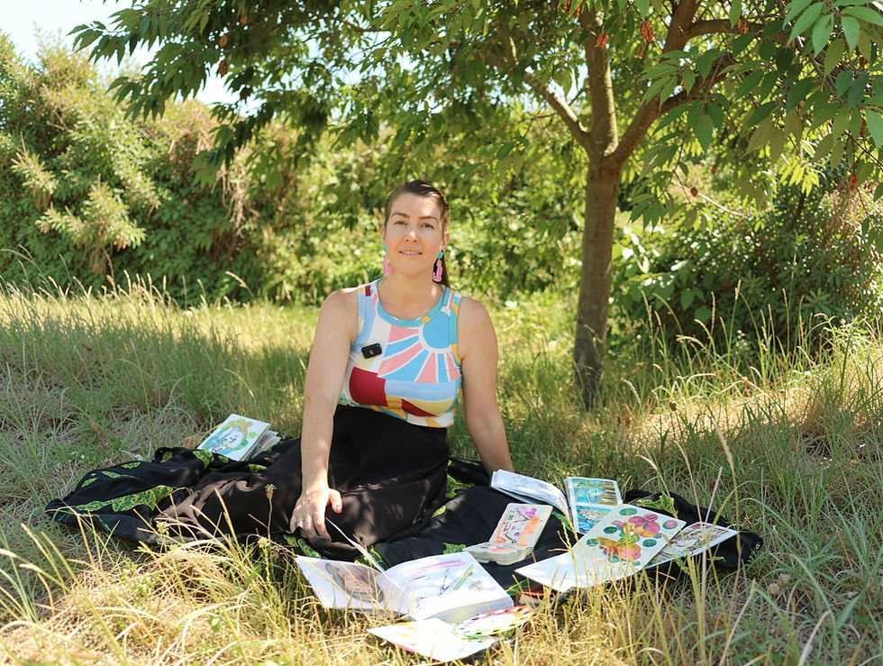 Woman sitting on a blanket under a tree in a grassy garden, surrounded by colorful illustrated cards, smiling calmly.