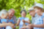 Group of elder friends playing cards together and laughing while outdoors.