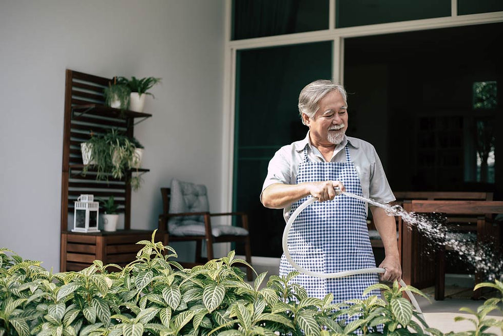 Elder man relaxing while watering his garden outside.