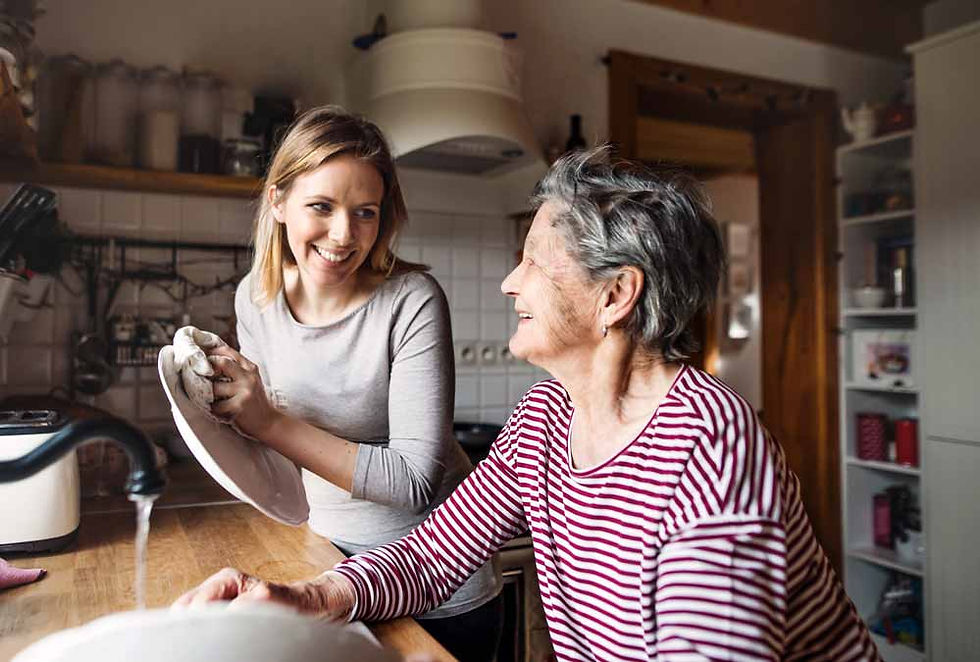 Elder grandmother and adult granddaughter laughing while washing dishes together.