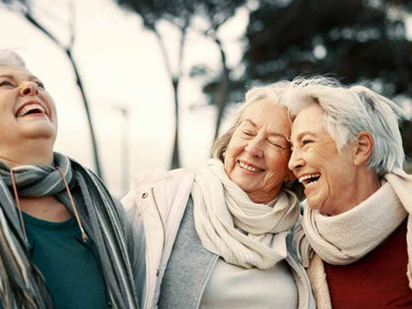 Three elder women laughing together while enjoying a walk together outdoors.