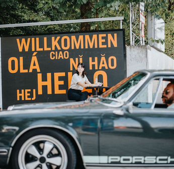 Ein grüner luftgekühlter Porsche 911 fährt an Welcome Schild der Münchner Werkvirtels vorbei.