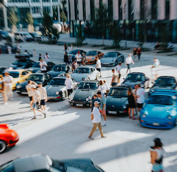 Die Parkfläche auf dem Werksviertel in München einer Veranstaltung auf der einige schöne Porsche Modelle stehen. Auf dem Platz sind auch einige Besucher zu sehen, die sich begeistert die Fahrzeuge ansehen. 