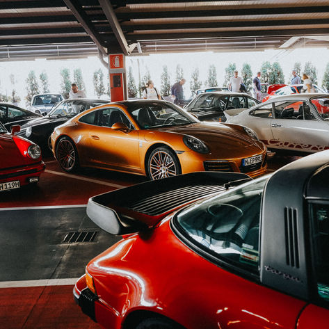 Ein Parkhaus mit vielen historischen Porsche 911. Im Vordergrund stehen zwei rote und ein orangenes Auto, es könnte sich fast um die Garage der Motorworld in Köln handeln.