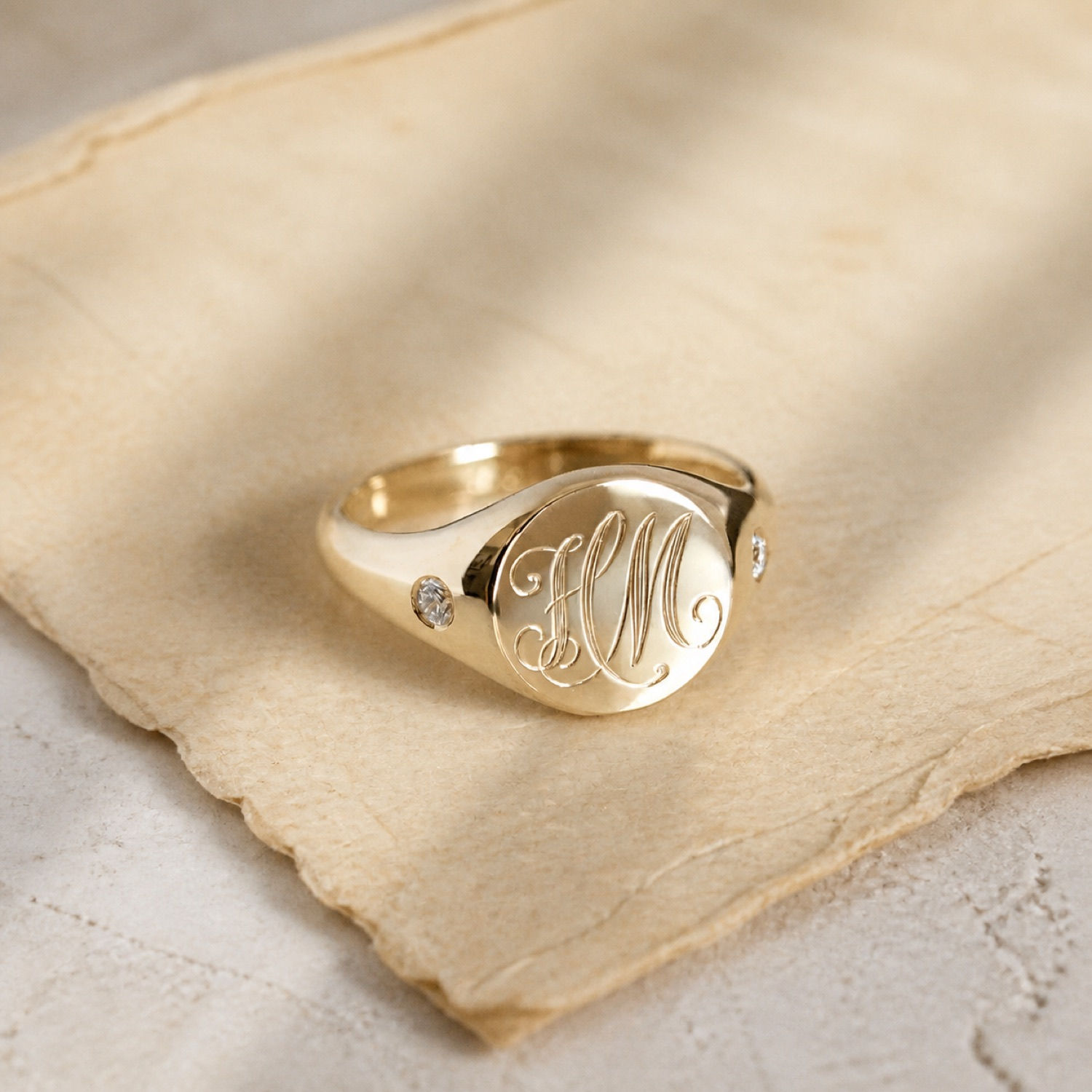 Classic diamond shoulder monogram signet ring on paper.
