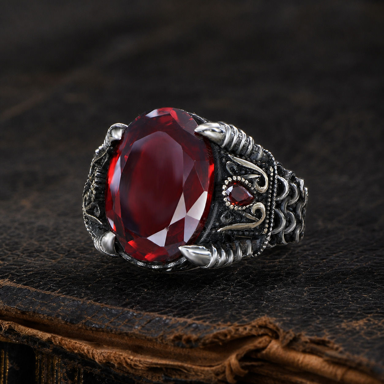 Oval Red Zircon Braided Chain Sterling Silver Men's Ring displayed on a black leather antique book