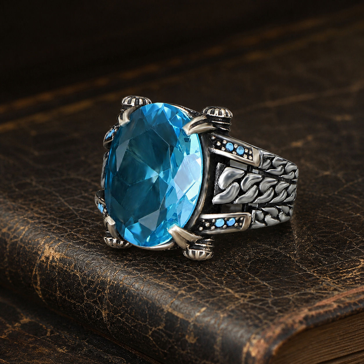 Oval Blue Topaz Braided Chain Sterling Silver Men's Ring displayed on a black leather antique book