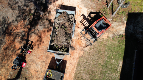 Kubota Skid Steer cleaning up trees and debris from above and loading into a dump trailer