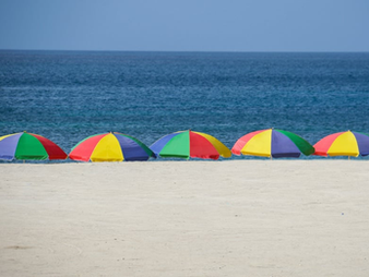 The image of five colorful umbrellas hovering over a long stretch of sand with a calm sea just beyond was taken by Nick Fewings.