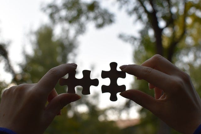Two puzzle pieces held in the air against the sky, having no context for the larger picture in which they fit.
