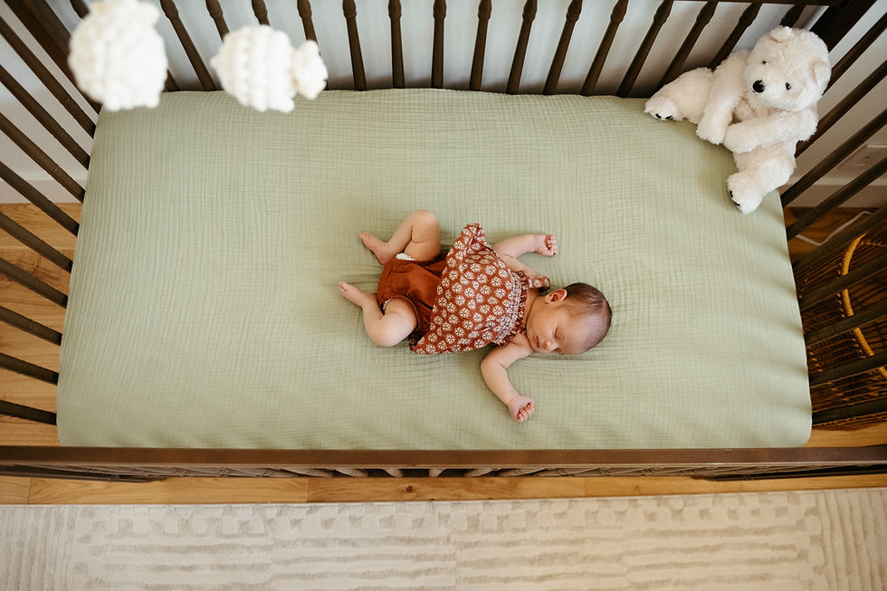 Baby sleeping in a crib on a green sheet, wearing a patterned outfit. A white teddy bear sits nearby. Peaceful nursery setting.