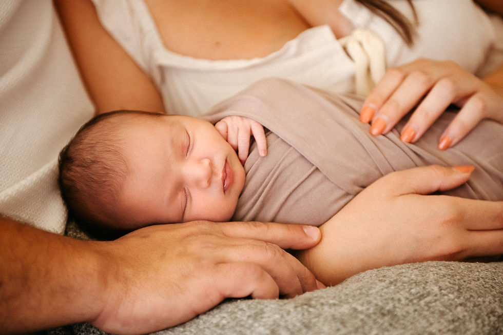 Sleeping baby swaddled in taupe blanket, cradled by adult hands. Peaceful setting with soft lighting and gentle, caring touch.