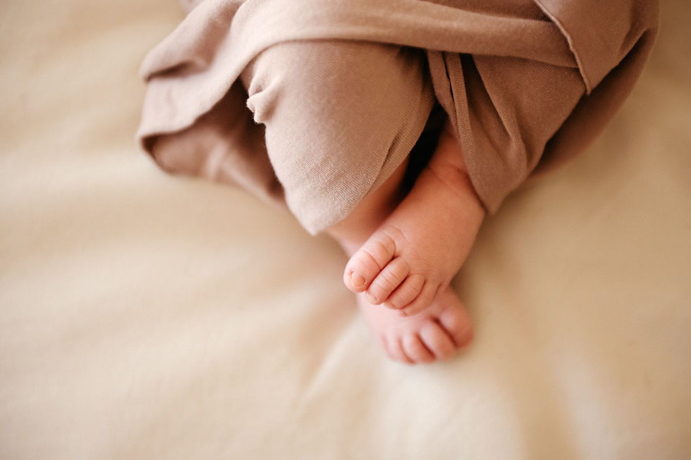 Baby feet in soft brown fabric, resting on a light cream blanket. Warm, cozy setting.
