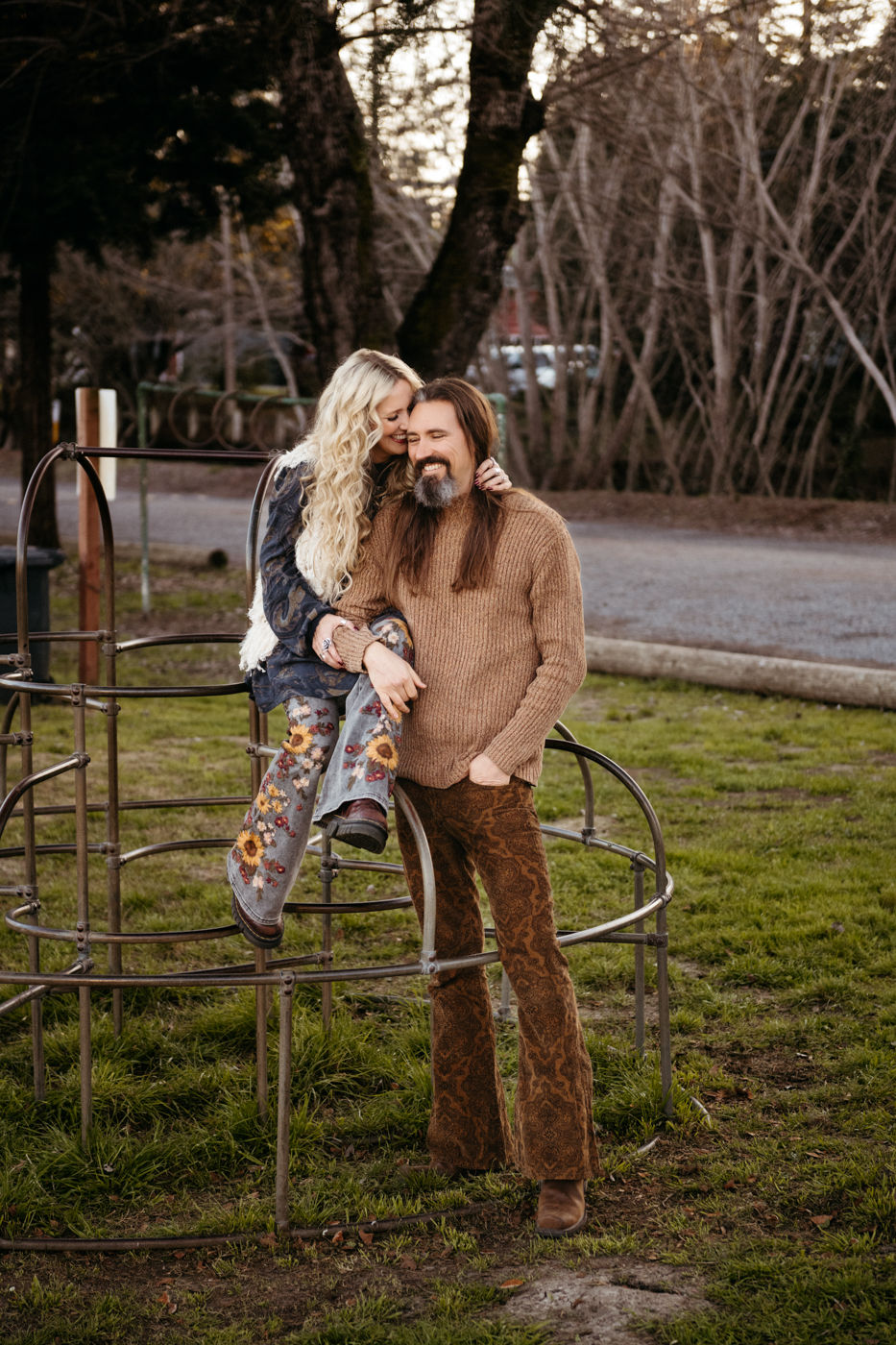 A cozy moment amid nature, as a couple enjoys a playful embrace on a vintage playground structure, surrounded by the tranquility of trees and grass.