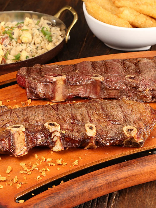 Costela assada com arroz, torresmo e fritas. Prato servido em tábua de madeira.