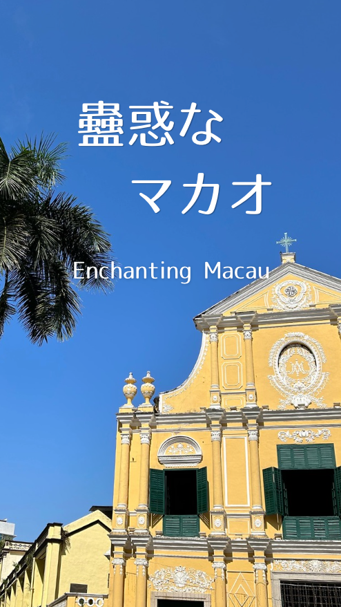 青空の下、ヤシの木と黄壁の教会風建築。白字で蠱惑な マカオ、Enchanting Macauと表示。