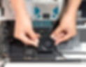 Eine Luftaufnahme von zwei Händen, die an einem Computer mit Mac Studio arbeiten. Die Hände setzen ein kleines, ventilatorähnliches Teil in das Gehäuse des Computers ein.