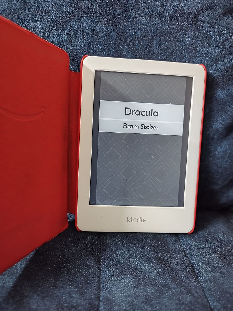Kindle e-reader in a red case on blue fabric, displaying Dracula by Bram Stoker.