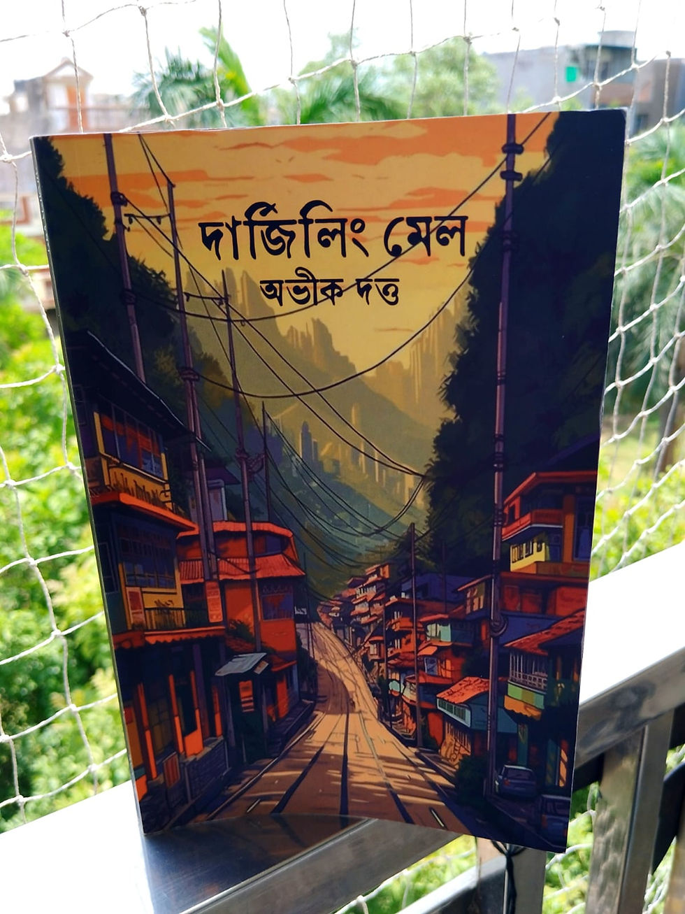 Book cover with Bengali text দার্জিলিং মেল (Darjeeling Mail), showing a colorful hill town street at sunset with power lines.