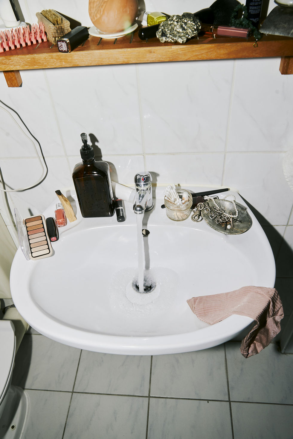 Weißes Waschbecken mit Kosmetik, Pflegeprodukten und persönlichen Gegenständen in einem individuell gestalteten Badezimmer.