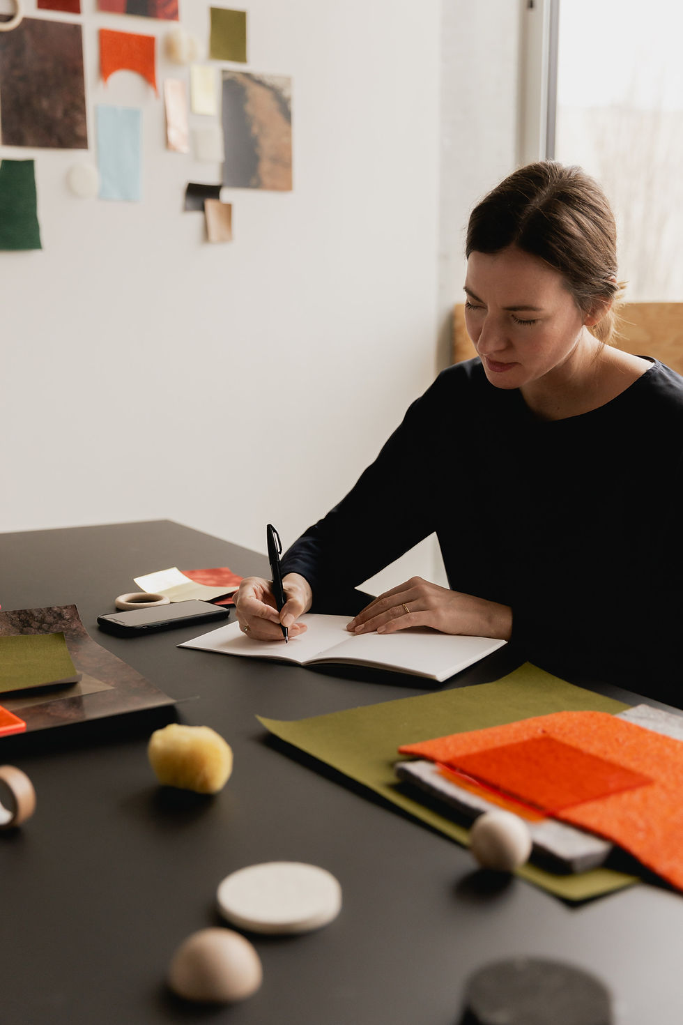 Designerin zeichnet an einem Arbeitstisch zwischen Farb- und Materialmustern eine Entwurfsskizze für ein Raumkonzept.
