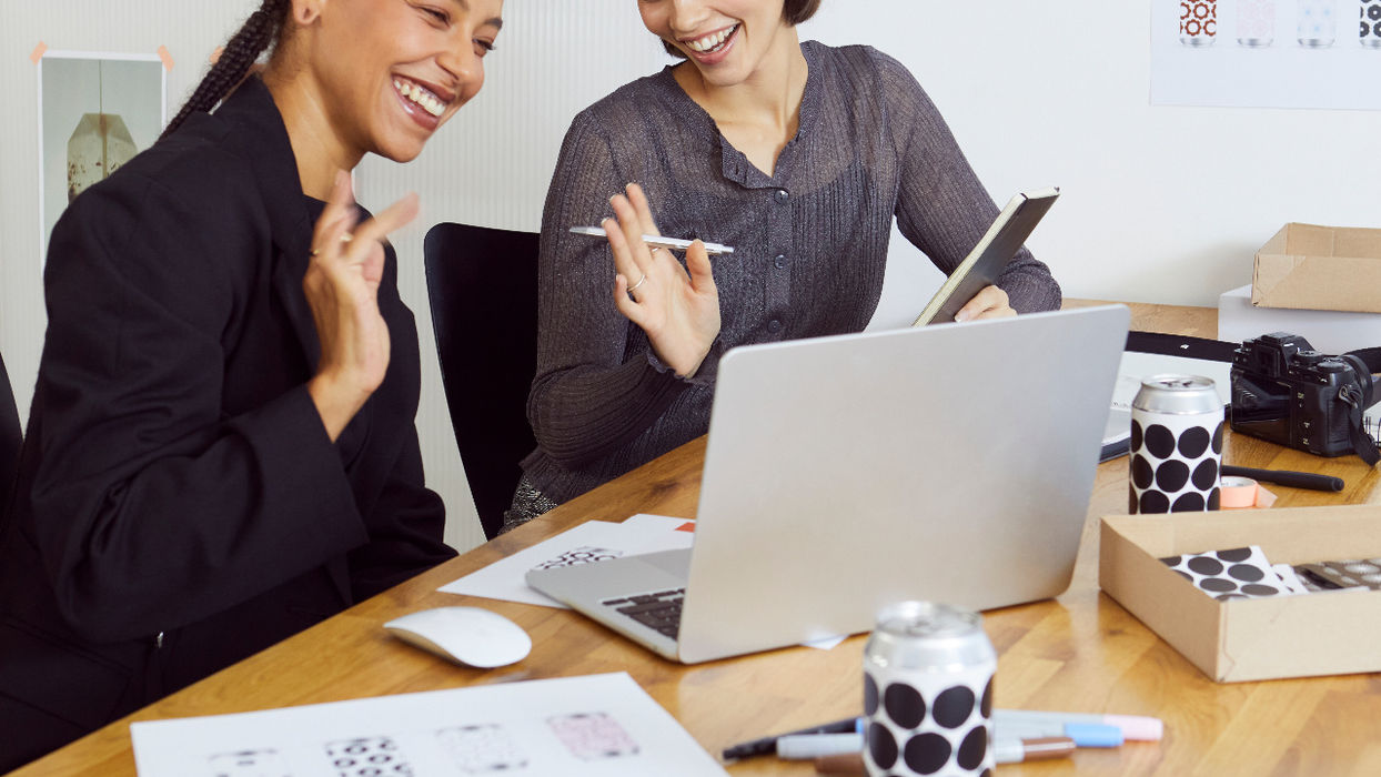 Zwei Personen betrachten gemeinsam einen Laptop zwischen Bildern und Arbeitsunterlagen.