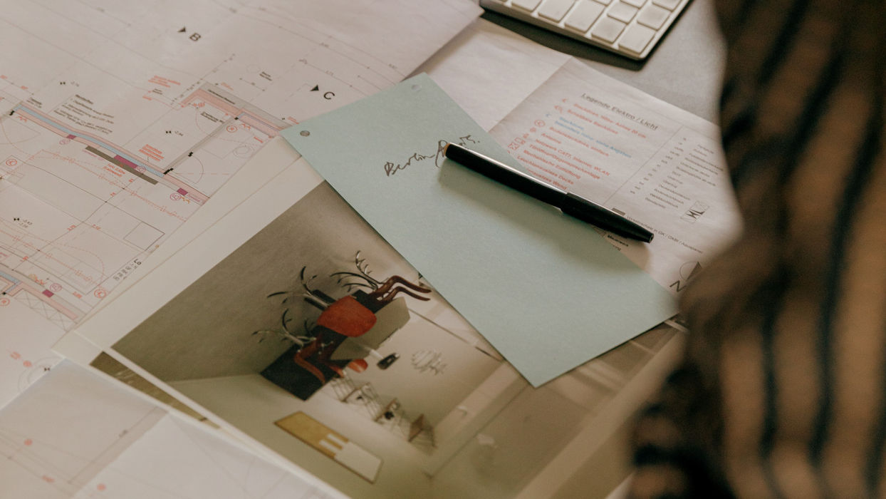 Arbeitsplatz mit Grundrissen, Raumvisualisierung, Notizen und Computer zur Ausarbeitung eines vollständigen Interior-Design-Konzepts.
