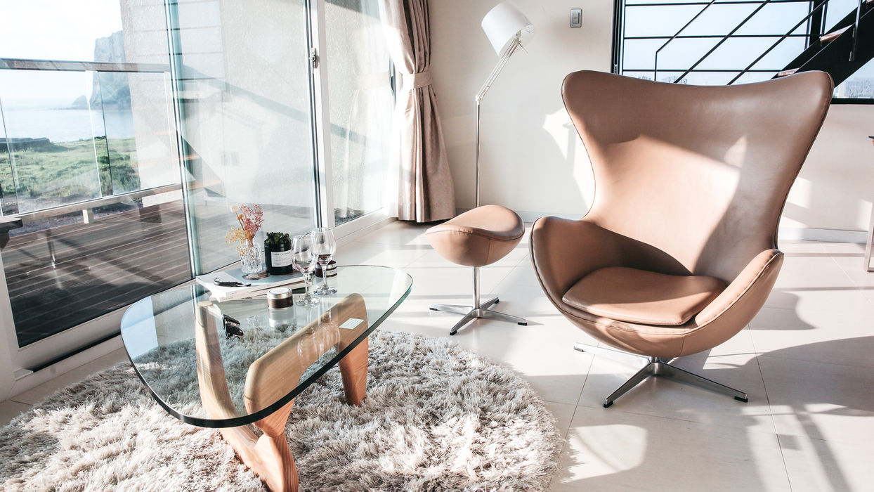 Heller Wohnbereich mit Ledersessel, Glastisch und großflächiger Fensterfront – modernes Interior Design für eine hochwertige Immobilienpräsentation.