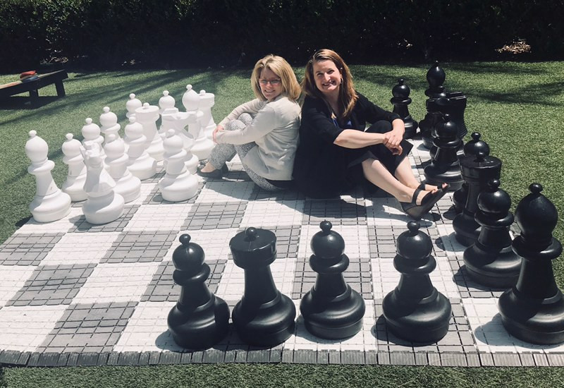 Catina O'Leary and Amy Waterman sit back to back on a life-size chess board, surrounded by large chess pieces