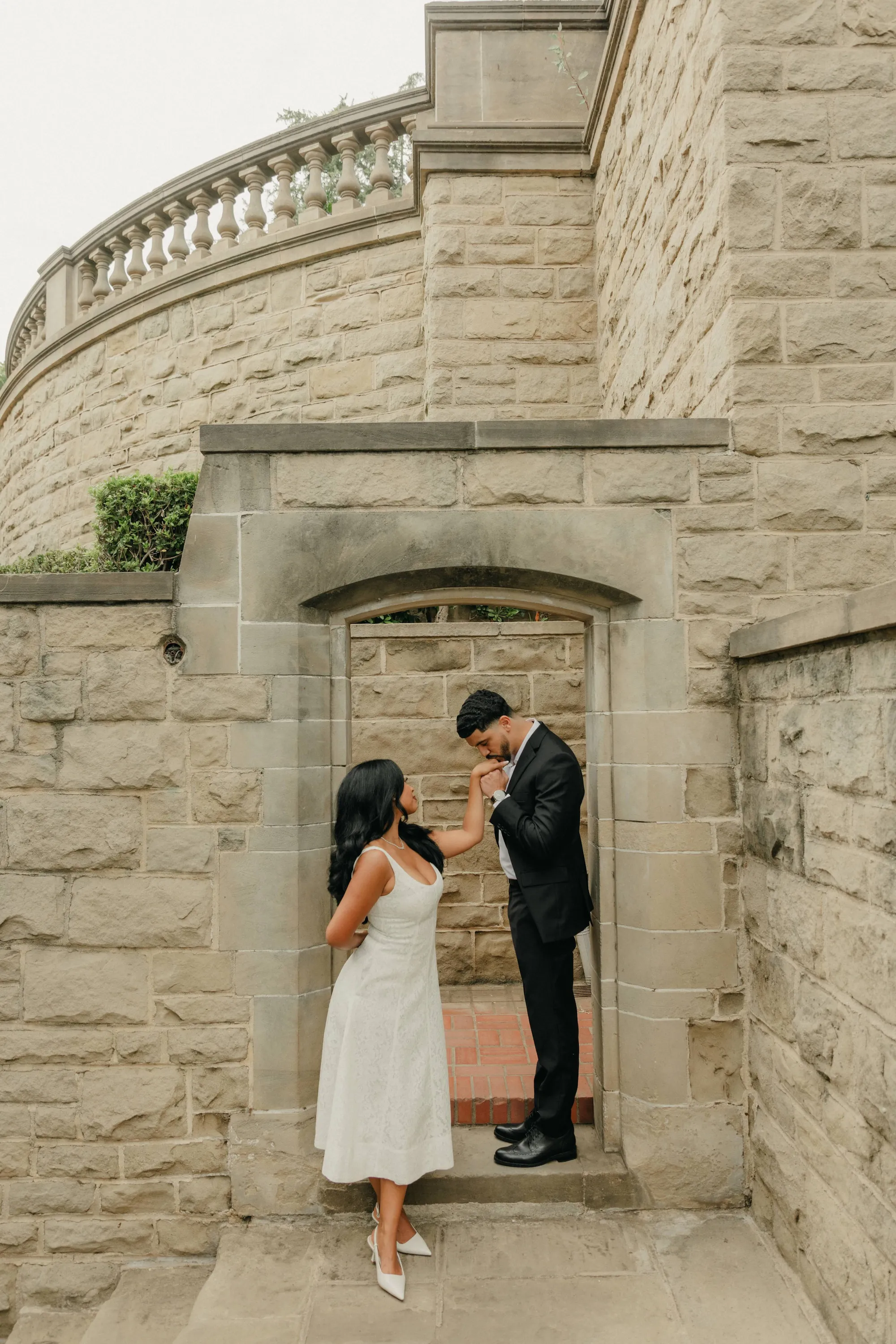engagement photo outfits at Greystone Mansion Beverly Hills, couple in black suit and white midi dress in stone archway