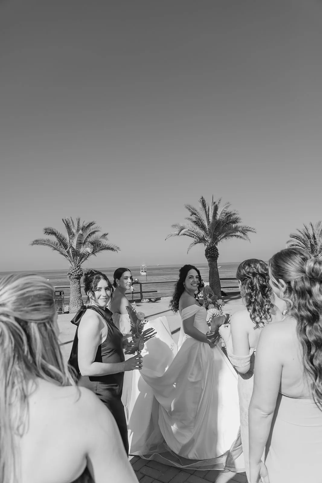 Bride surrounded by her bridesmaids outside the Catalina Island Casino, palm trees in the background, black and white
