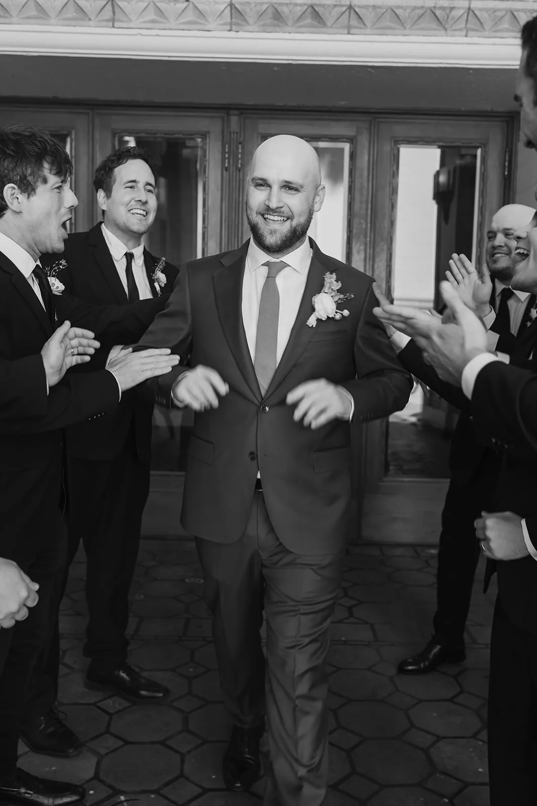 Groom laughing and dancing through a groomsmen tunnel at the Catalina Island Casino wedding entrance, black and white