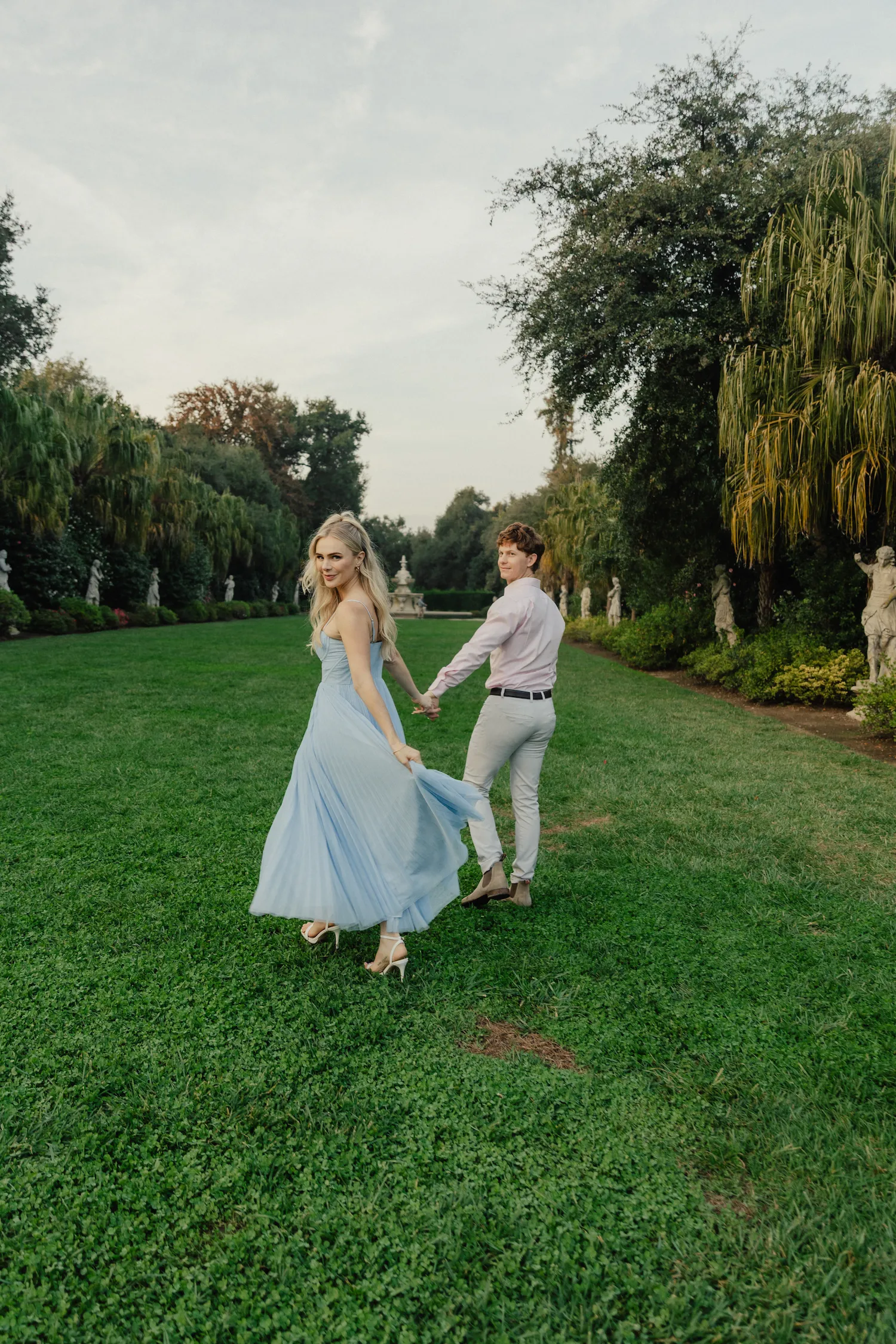 engagement photo outfits at the Huntington Library San Marino, couple in blue flowy dress and pink shirt dancing on the garden lawn