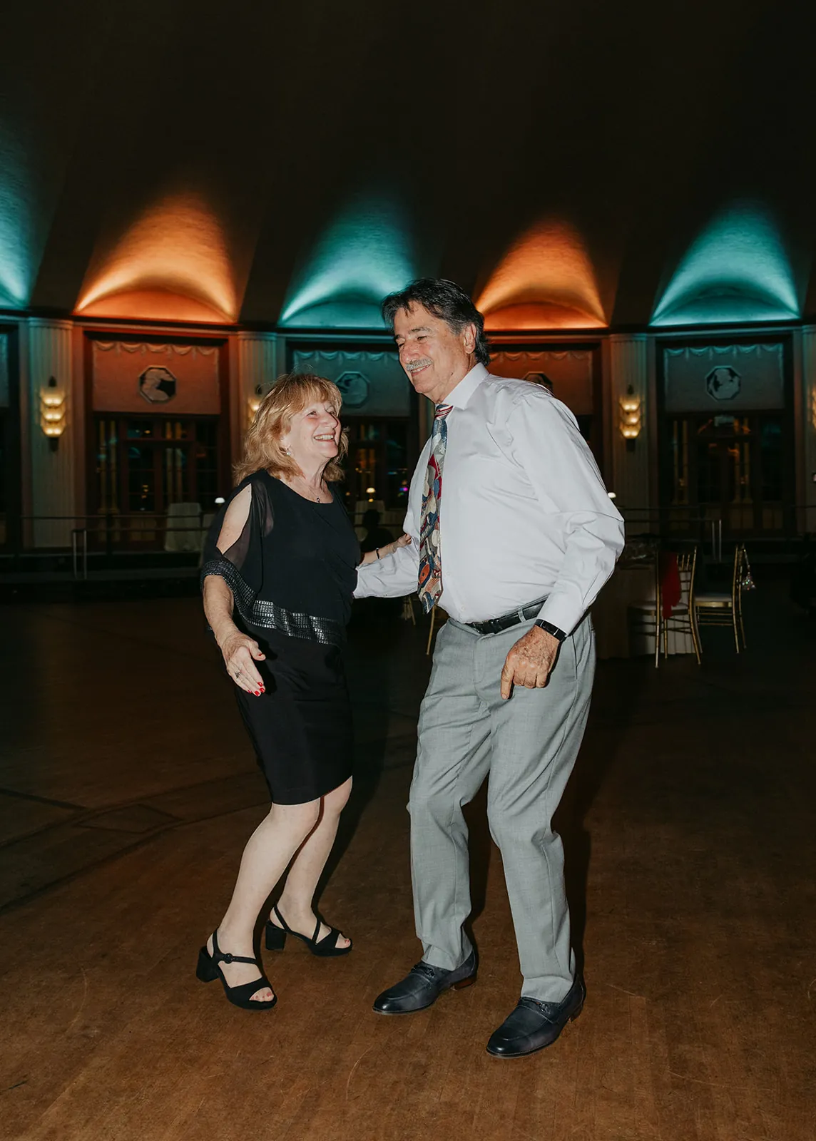 Couple dancing on the Catalina Island Casino Ballroom floor near the end of the night, teal and amber uplighting glowing behind them