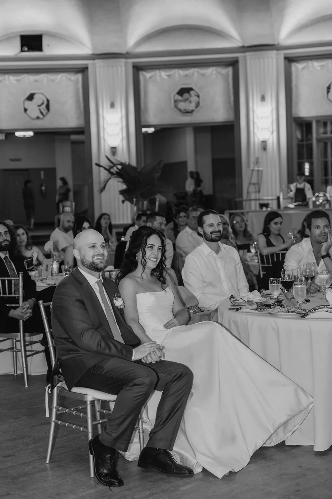 Bride and groom smiling at the sweetheart table during wedding speeches in the Catalina Island Casino Ballroom, black and white