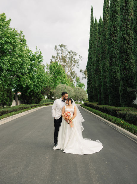 Wide shot of bride and groom walking down a cypress tree-lined road.