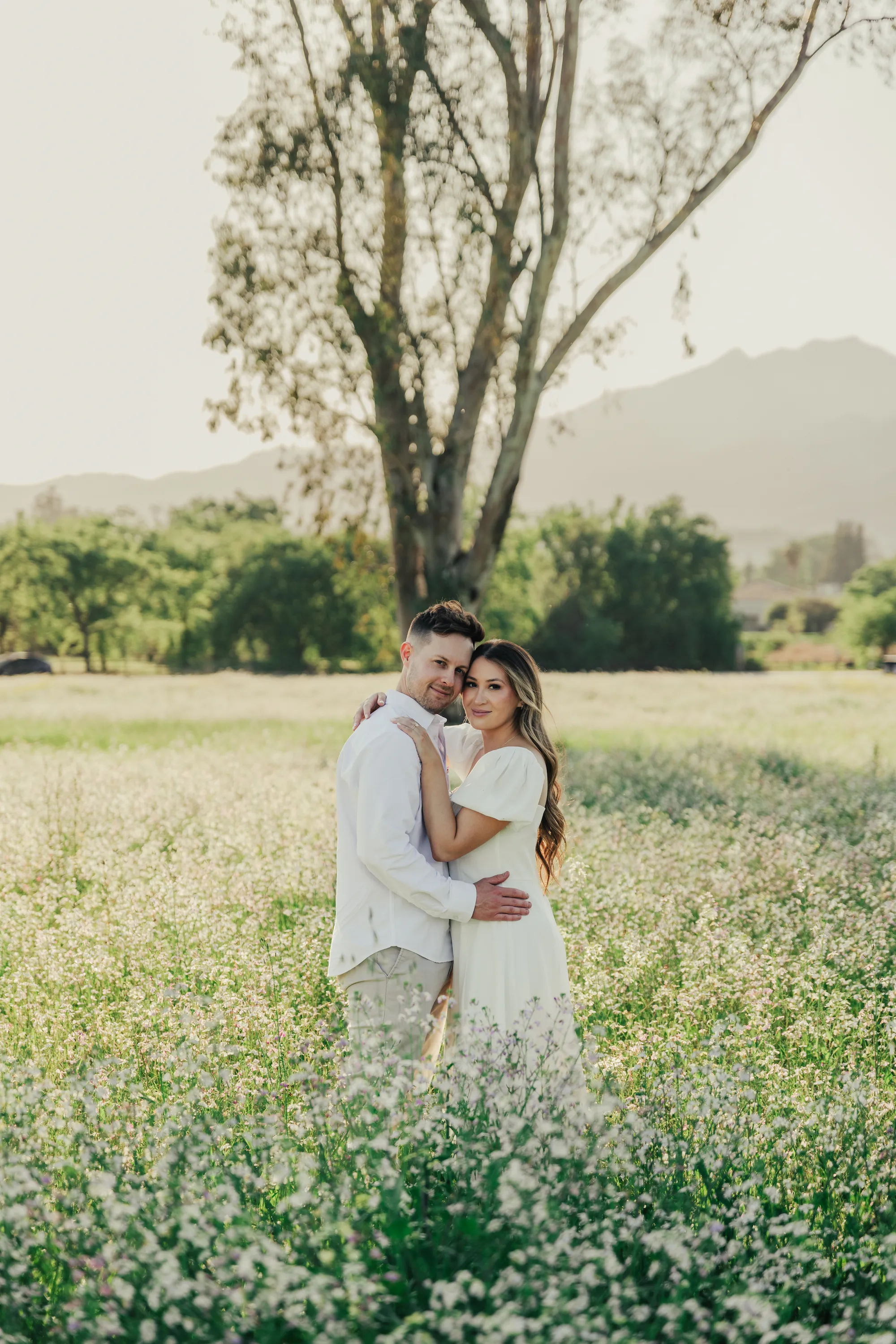 engagement photo outfits in Ojai California, couple in white dress embracing in a wildflower field with soft natural light