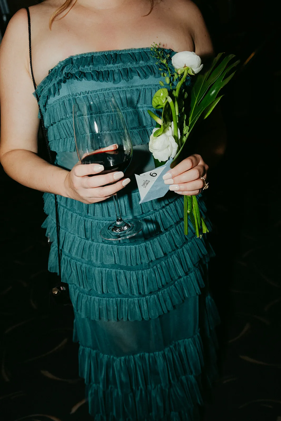 Bridesmaid holding a white floral bouquet, wine glass, and sailboat escort card at the Catalina Island Casino wedding cocktail hour