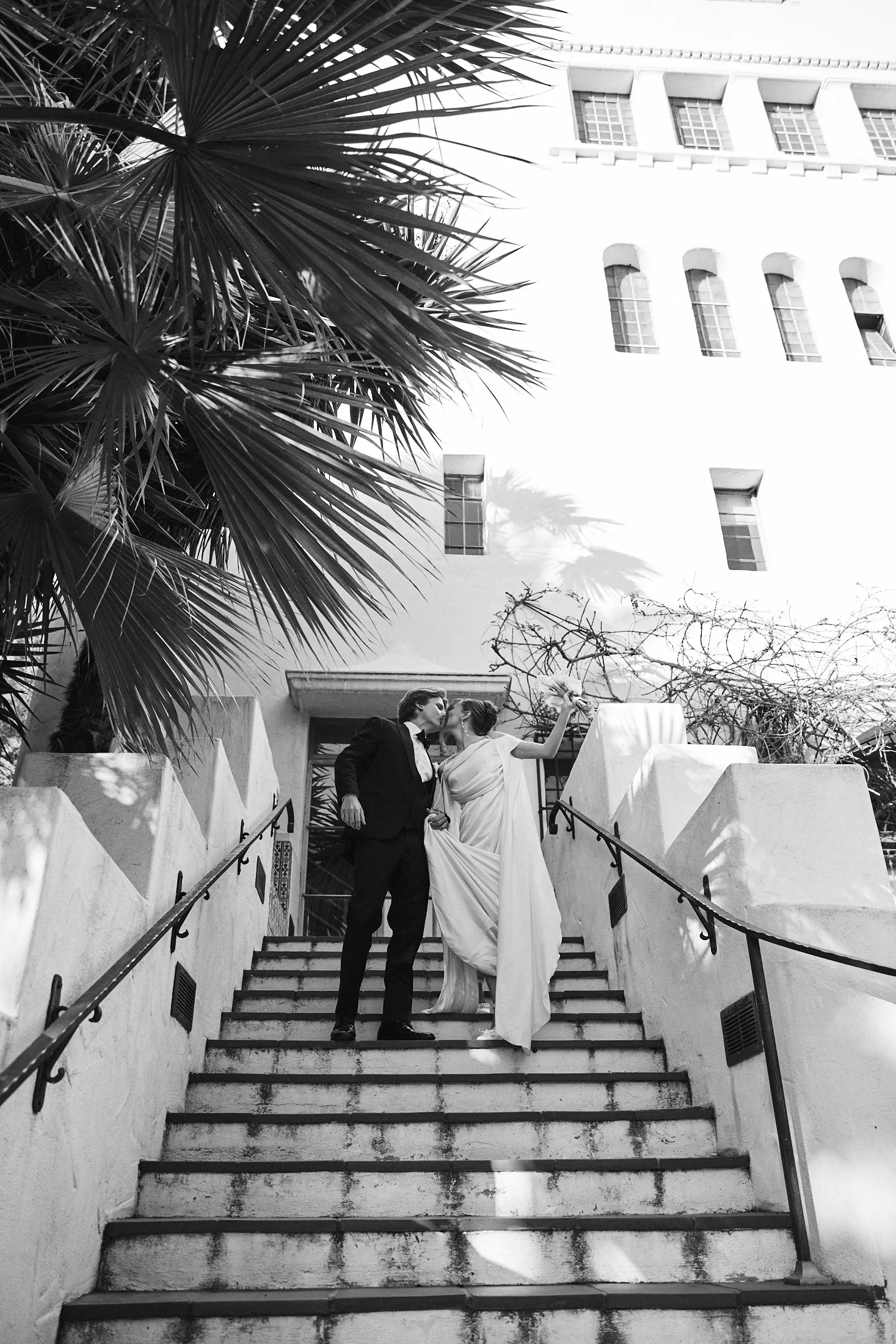 Black and white photo of bride walking up the exterior stairs toward her groom at the Santa Barbara Courthouse wedding