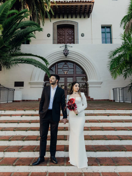 Bride and groom standing on the courthouse steps with red bouquet at their Santa Barbara courthouse wedding