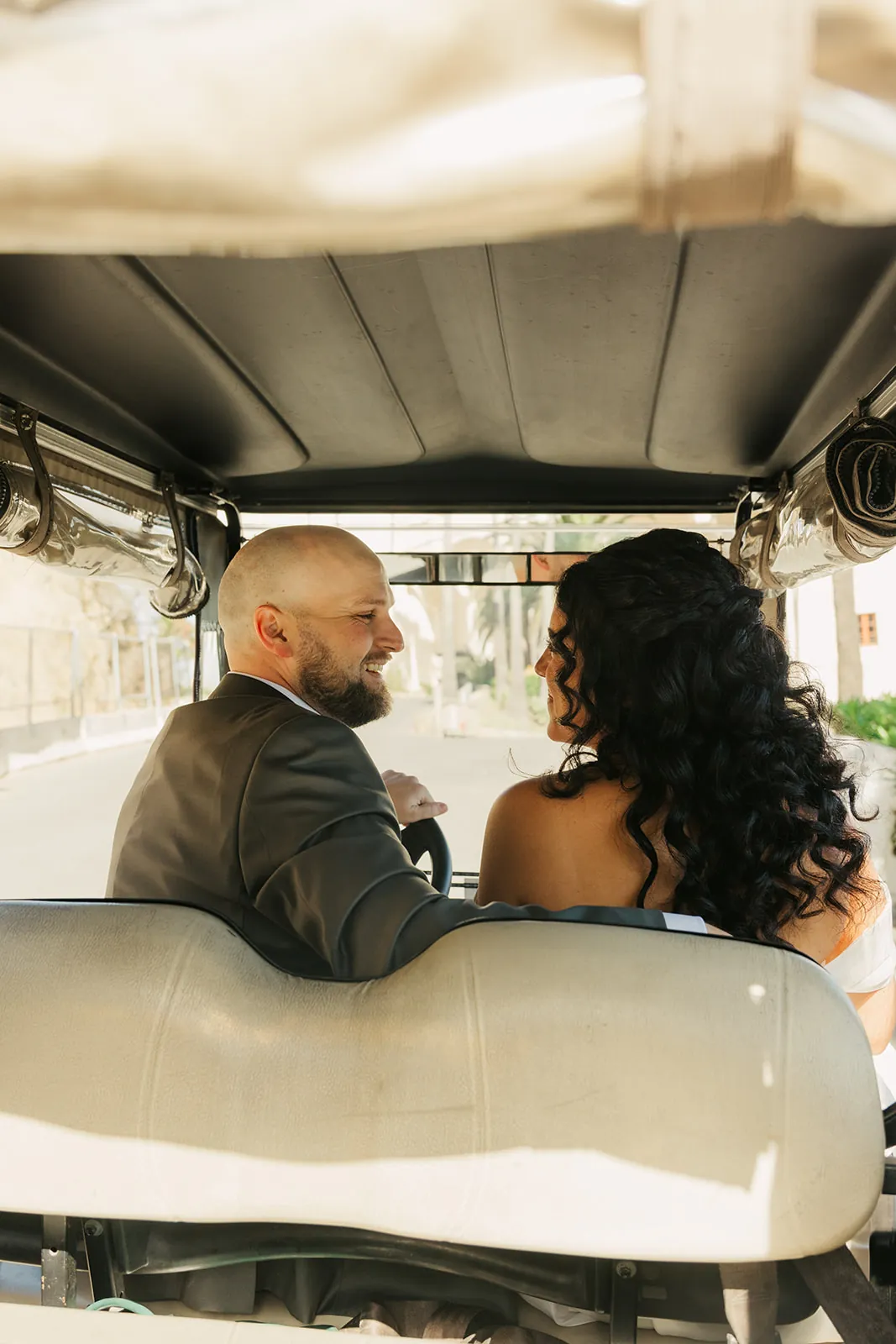 Bride and groom facing each other laughing in a golf cart in Avalon, Catalina Island — the only way to get around town on their wedding day